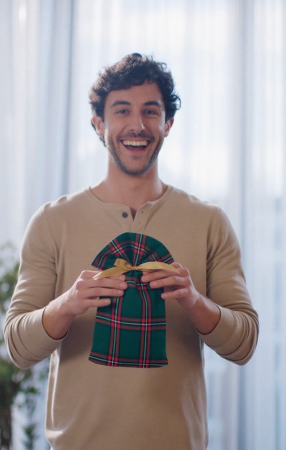 Man holding a green plaid bag in front of a light curtain background
